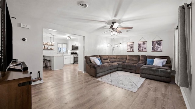 living room with ceiling fan, sink, and light hardwood / wood-style floors