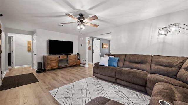 living room with light hardwood / wood-style flooring, a barn door, and ceiling fan