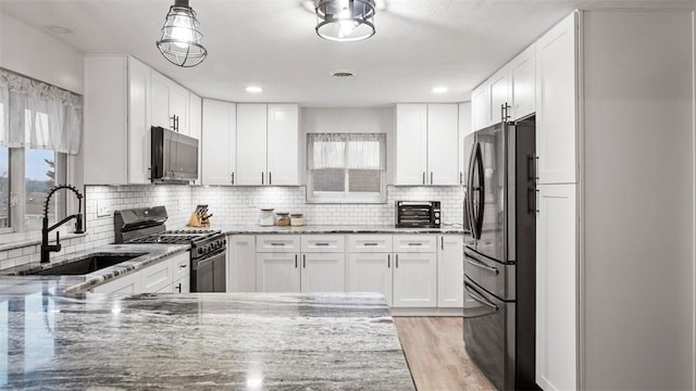 kitchen with sink, black refrigerator, light stone counters, white cabinets, and gas range