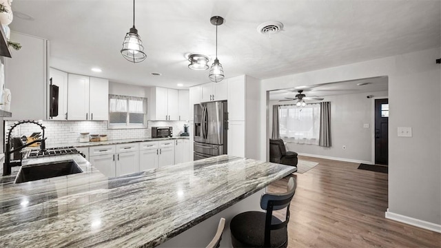 kitchen with a breakfast bar, sink, dark stone countertops, stainless steel fridge, and kitchen peninsula