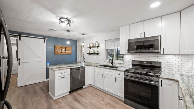 kitchen featuring sink, appliances with stainless steel finishes, kitchen peninsula, white cabinets, and a barn door