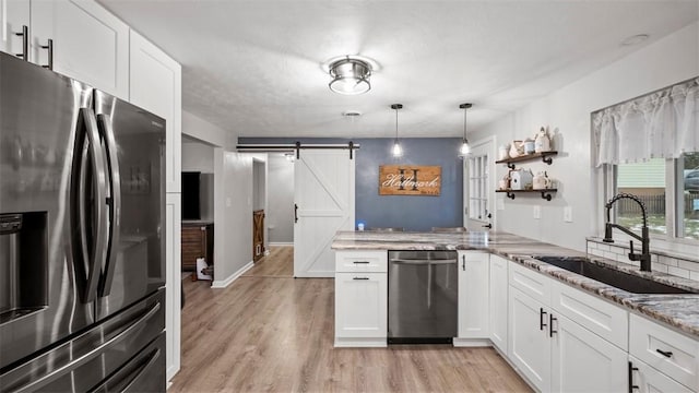 kitchen with appliances with stainless steel finishes, a barn door, sink, and white cabinets