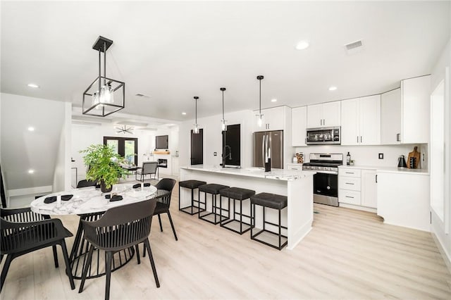 kitchen with decorative light fixtures, white cabinets, a large island, stainless steel appliances, and light hardwood / wood-style flooring