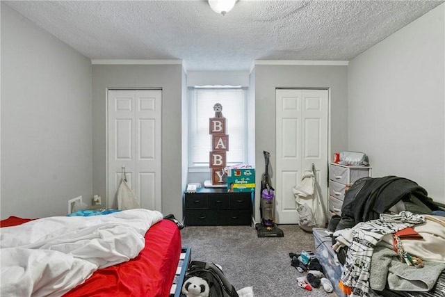 bedroom featuring crown molding, carpet flooring, a textured ceiling, and two closets