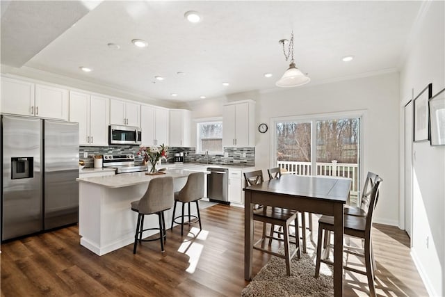 kitchen featuring stainless steel appliances, a center island, white cabinets, and decorative light fixtures