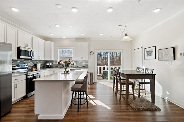 kitchen with pendant lighting, appliances with stainless steel finishes, a center island, tasteful backsplash, and white cabinets