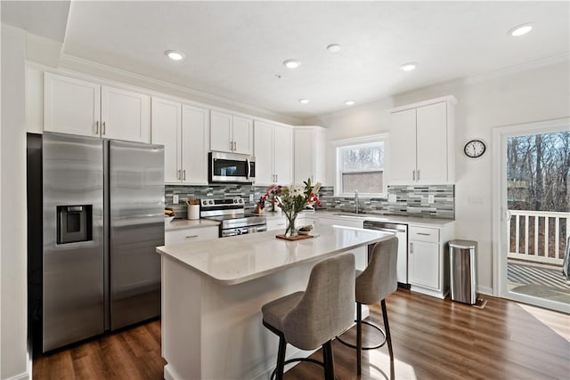 kitchen with a kitchen bar, white cabinetry, appliances with stainless steel finishes, dark hardwood / wood-style floors, and a kitchen island