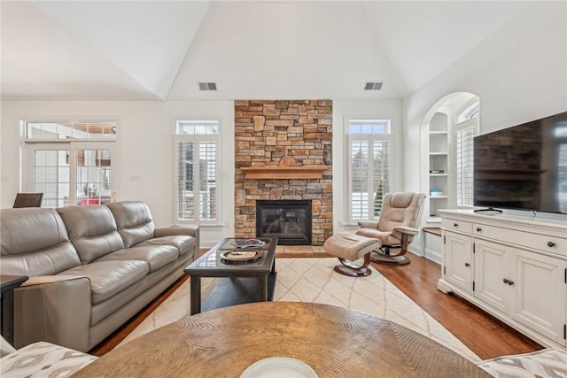 living room with high vaulted ceiling, light hardwood / wood-style flooring, a fireplace, and built in shelves