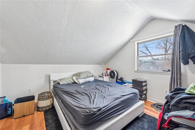 bedroom featuring wood-type flooring, vaulted ceiling, and a textured ceiling