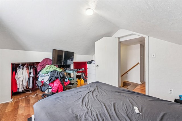 bedroom with wood-type flooring, lofted ceiling, and a textured ceiling