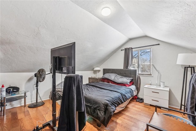 bedroom with lofted ceiling, light hardwood / wood-style floors, and a textured ceiling