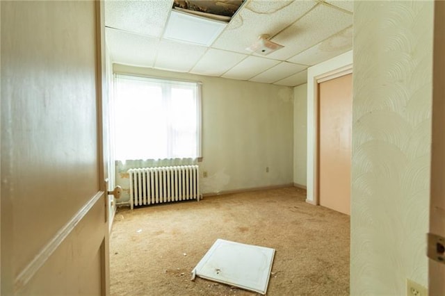 carpeted spare room with radiator and a paneled ceiling