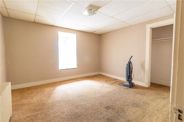 unfurnished bedroom with a closet, radiator heating unit, light carpet, and a drop ceiling