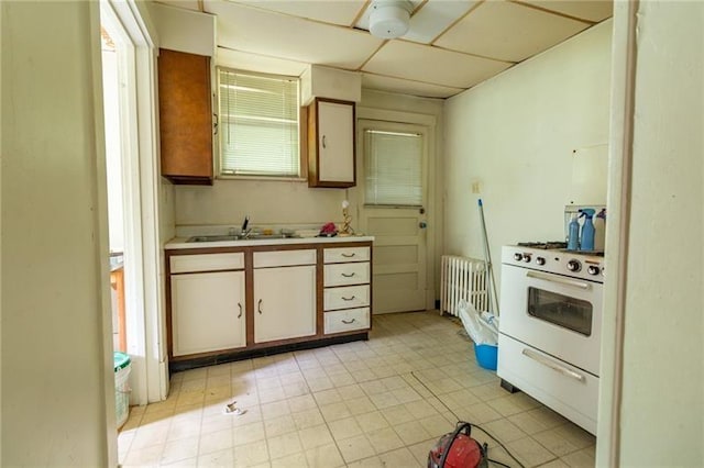 kitchen with sink, radiator heating unit, a drop ceiling, and white stove