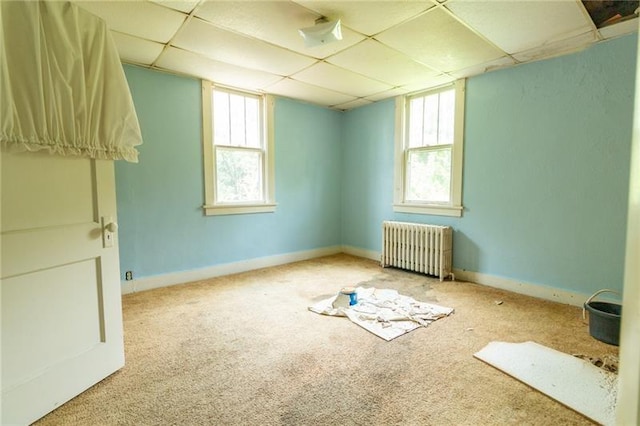 spare room with a paneled ceiling, radiator, and light carpet