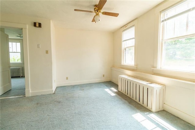 carpeted spare room featuring ceiling fan, radiator heating unit, and a wealth of natural light