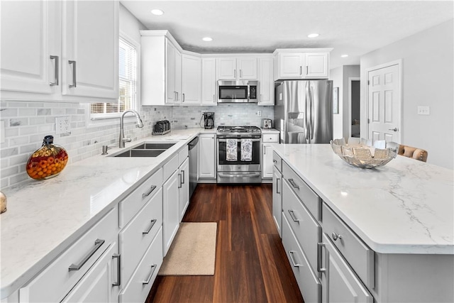 kitchen with white cabinetry, stainless steel appliances, sink, and light stone counters