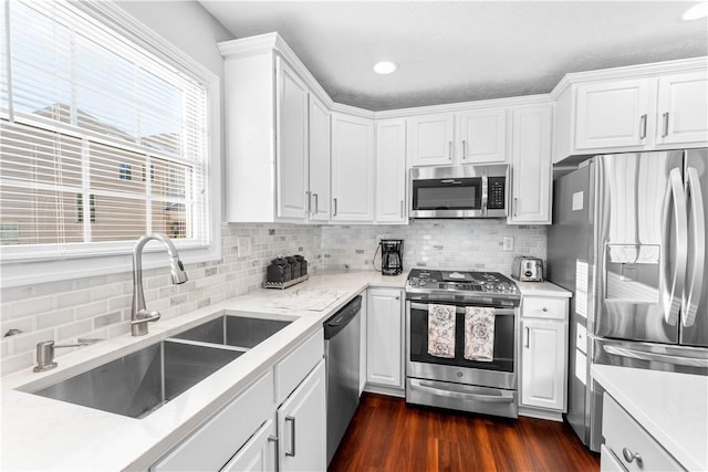 kitchen with appliances with stainless steel finishes, dark hardwood / wood-style floors, white cabinetry, sink, and backsplash