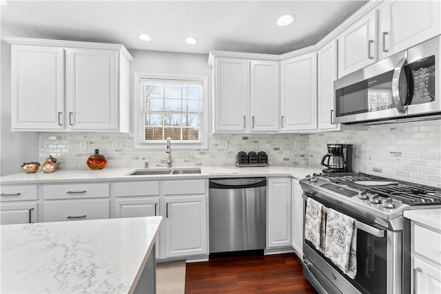 kitchen with sink, appliances with stainless steel finishes, white cabinets, dark hardwood / wood-style flooring, and decorative backsplash