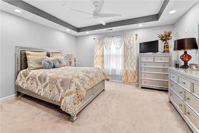 bedroom with light carpet, ceiling fan, and a tray ceiling