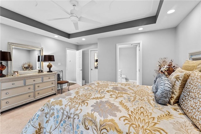 bedroom with ceiling fan, light colored carpet, a raised ceiling, and ensuite bath