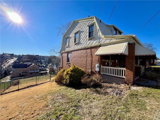 view of side of home featuring a lawn, a gambrel roof, fence, a porch, and brick siding