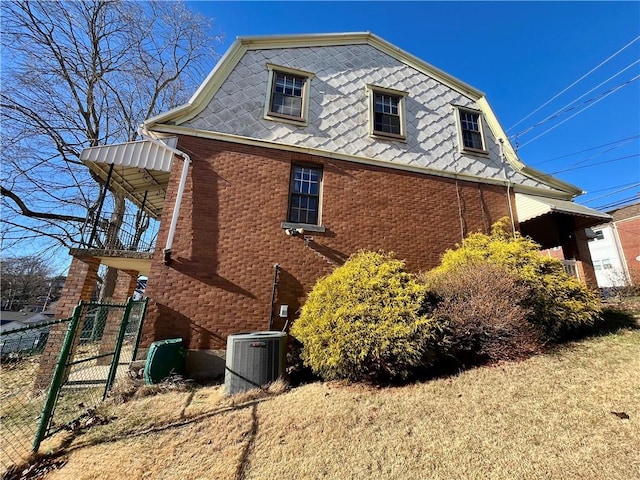 view of side of property featuring fence, mansard roof, central AC, and brick siding