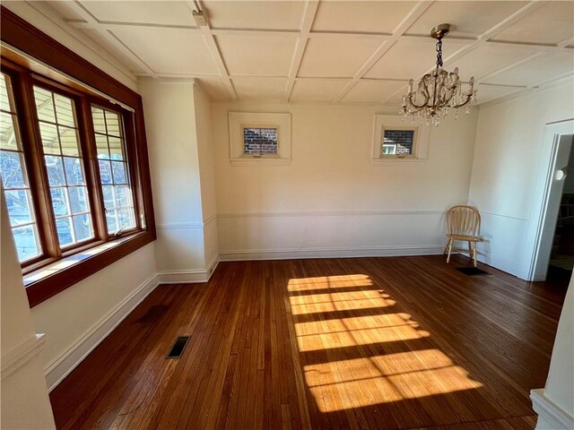 unfurnished dining area featuring an inviting chandelier, dark wood-type flooring, and coffered ceiling