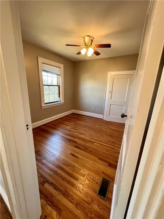 spare room with baseboards, visible vents, ceiling fan, and wood finished floors