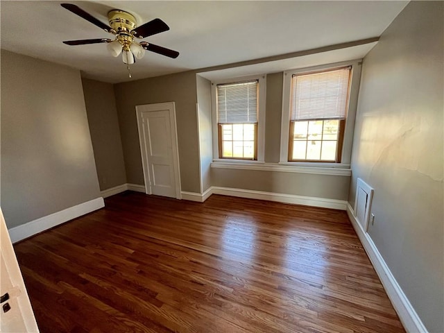 empty room with visible vents, baseboards, dark wood finished floors, and a ceiling fan