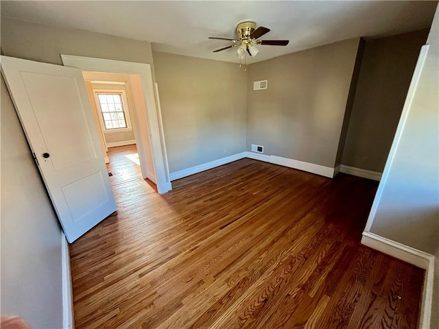 unfurnished bedroom featuring dark wood-style floors, visible vents, baseboards, and a ceiling fan