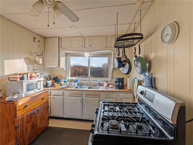 kitchen with stainless steel gas range oven, sink, ceiling fan, and wood walls