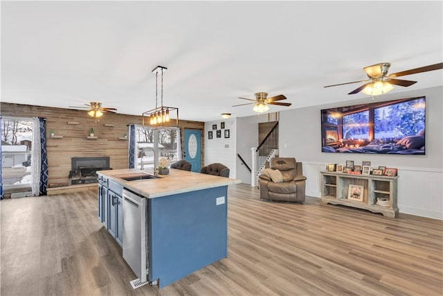 kitchen with decorative light fixtures, sink, stainless steel dishwasher, a center island with sink, and light hardwood / wood-style flooring