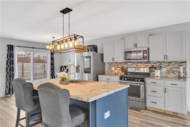 kitchen with light stone counters, hanging light fixtures, light wood-type flooring, an island with sink, and stainless steel appliances