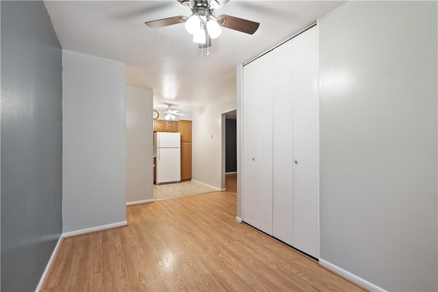 unfurnished bedroom with a closet, white fridge, ceiling fan, and light hardwood / wood-style flooring