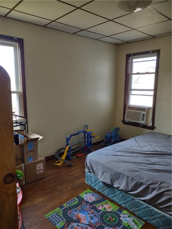 bedroom featuring cooling unit, hardwood / wood-style floors, multiple windows, and a drop ceiling