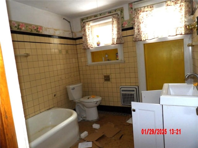 bathroom featuring tile walls, heating unit, vanity, toilet, and a bathing tub