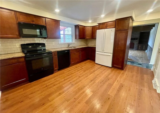 kitchen with sink, light hardwood / wood-style flooring, backsplash, light stone countertops, and black appliances