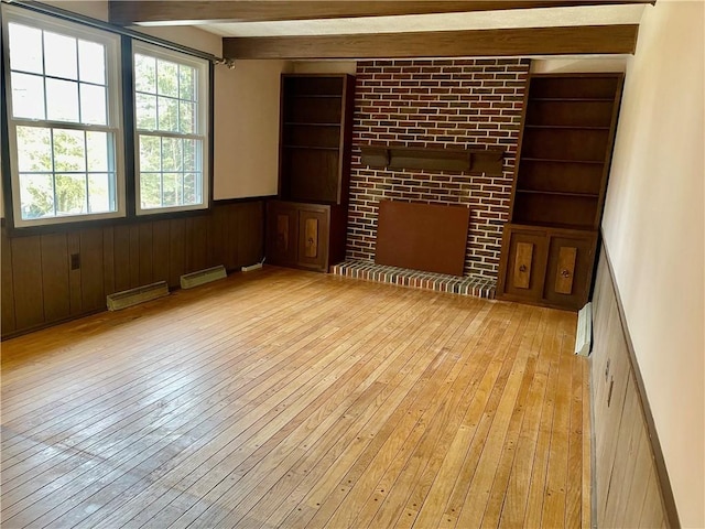 unfurnished room featuring a brick fireplace, light hardwood / wood-style flooring, beam ceiling, and built in shelves