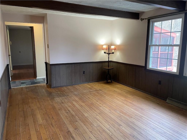 unfurnished room with a baseboard radiator, beam ceiling, light hardwood / wood-style floors, and a textured ceiling