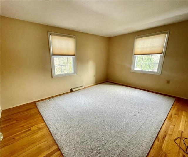 unfurnished room featuring a healthy amount of sunlight, hardwood / wood-style floors, and baseboard heating