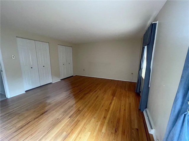 unfurnished bedroom featuring hardwood / wood-style flooring, a baseboard heating unit, and two closets