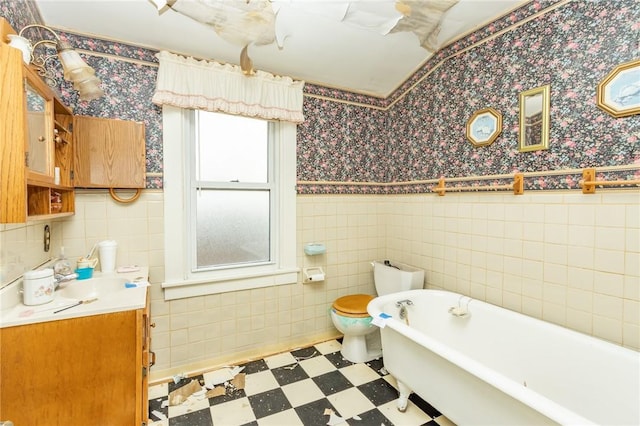 bathroom with a tub to relax in, toilet, tile walls, and vanity