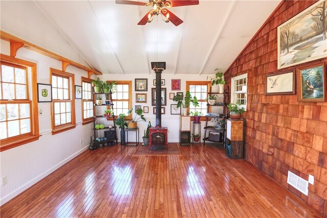 interior space with visible vents, baseboards, vaulted ceiling, wood-type flooring, and a wood stove