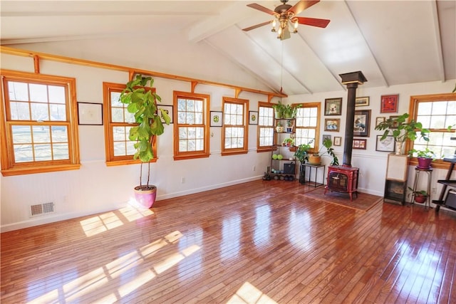 interior space featuring a wood stove, vaulted ceiling with beams, wood-type flooring, and visible vents