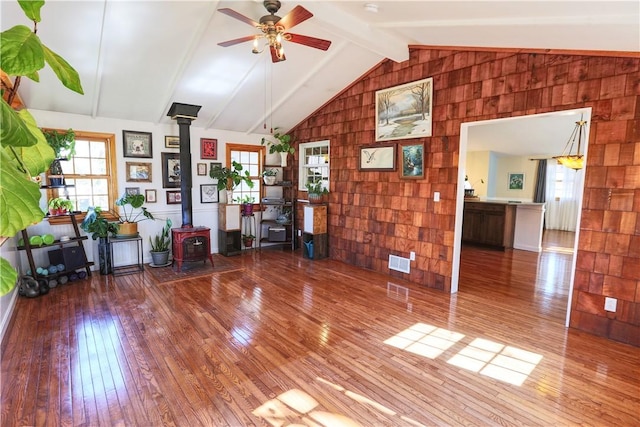 unfurnished living room with visible vents, hardwood / wood-style floors, lofted ceiling with beams, and a wood stove