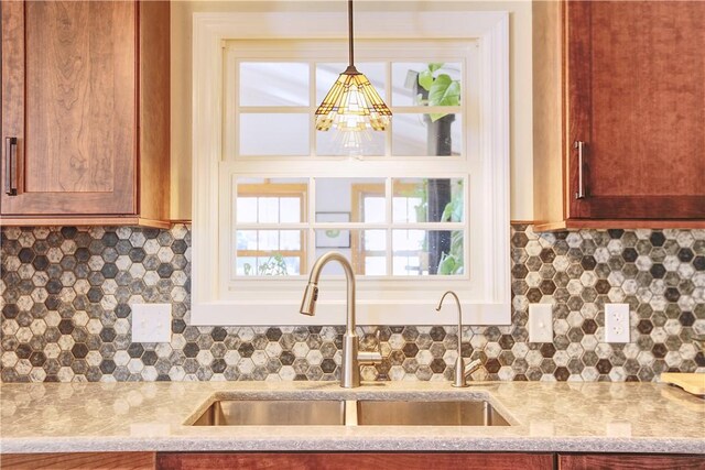 kitchen with pendant lighting, a notable chandelier, backsplash, a sink, and light stone countertops