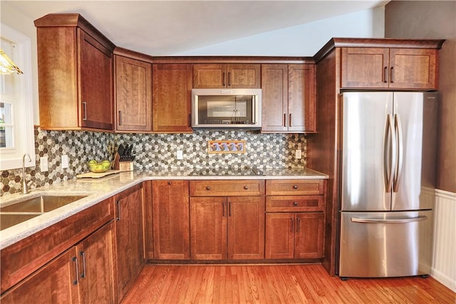 kitchen featuring vaulted ceiling, stainless steel appliances, light wood finished floors, and a sink