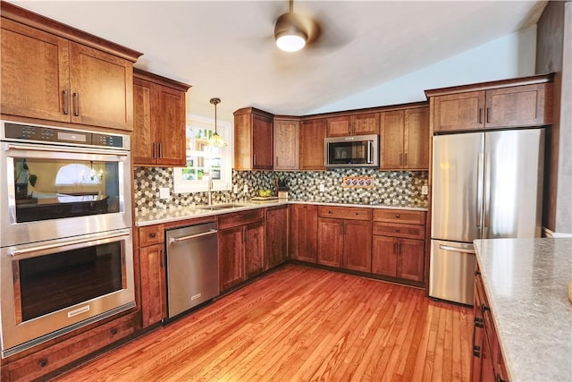 kitchen with stainless steel appliances, a sink, vaulted ceiling, light wood-type flooring, and backsplash