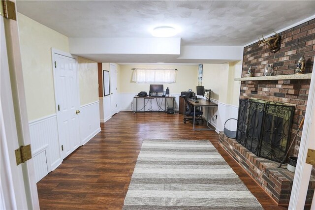 office space featuring wainscoting, wood finished floors, and a brick fireplace